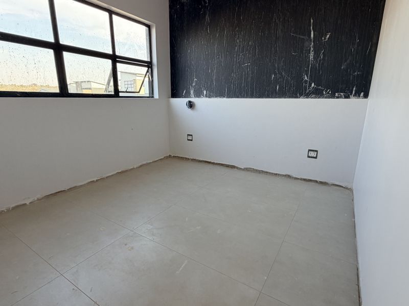 An empty bedroom featuring tiled flooring and large aluminium windows, currently requiring final finishing touches to the walls and skirting boards.