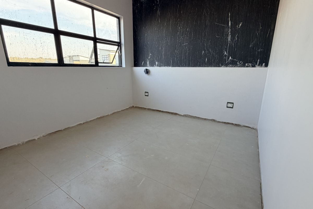 An empty bedroom featuring tiled flooring and large aluminium windows, currently requiring final finishing touches to the walls and skirting boards.