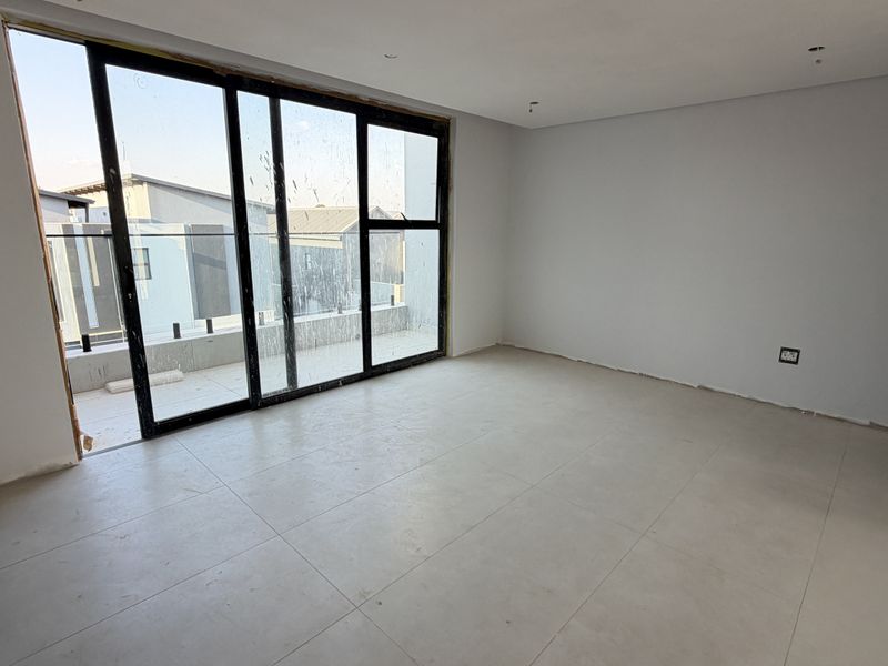 A spacious, empty bedroom featuring large sliding glass doors that open onto a balcony, finished with neutral floor tiles and clean wall surfaces.