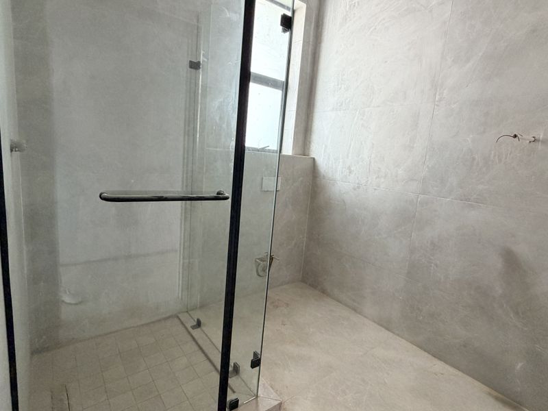 A partially completed bathroom featuring a glass shower enclosure, tiled walls and flooring, currently awaiting final finishes and fixtures.