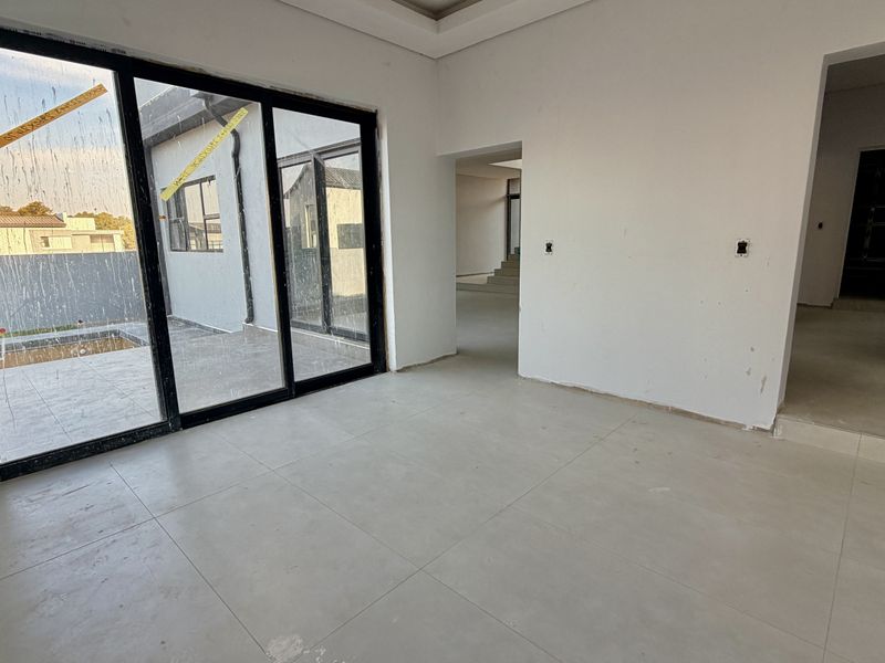 An empty, unfinished living area featuring large sliding glass doors leading to an outdoor patio, with neutral tiled flooring and modern architectural lines.