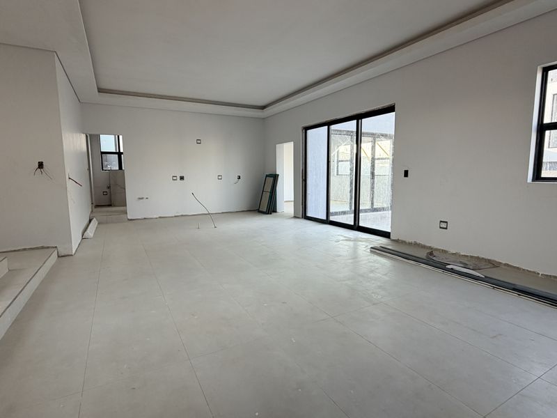 Spacious, open-plan living area in a new build, featuring large sliding glass doors, tiled floors, and a modern recessed ceiling design.