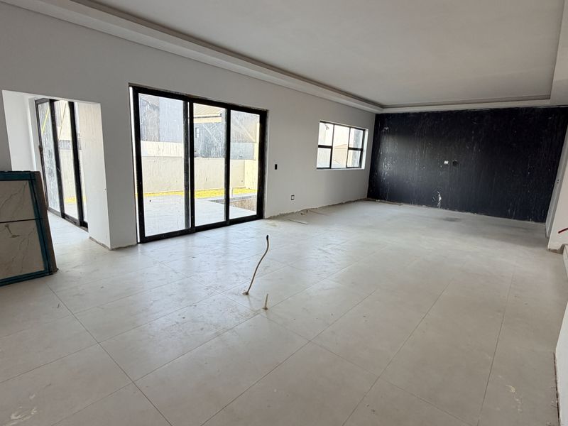 Spacious, open-plan living area featuring large sliding glass doors, neutral tiled flooring, and a striking black feature wall, currently in a final construction phase.