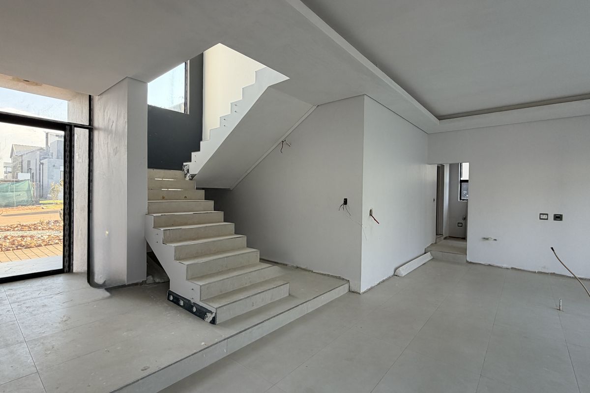 An open-plan living area under construction, featuring a modern staircase, tiled flooring, and recessed ceiling details, awaiting final finishes and electrical fixtures.