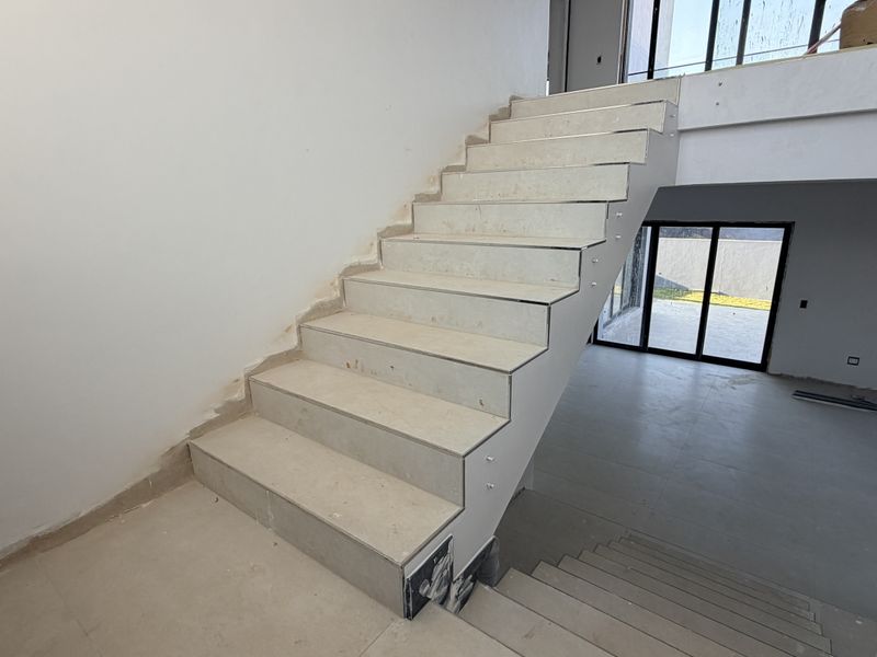 An unfinished open-plan hallway featuring a tiled staircase and large glass sliding doors leading to the exterior, currently in a construction phase.