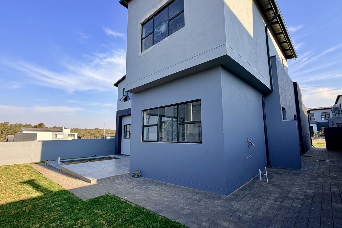 Rear view of a modern double-story house featuring a paved patio area, small lawn, and boundary walling.
