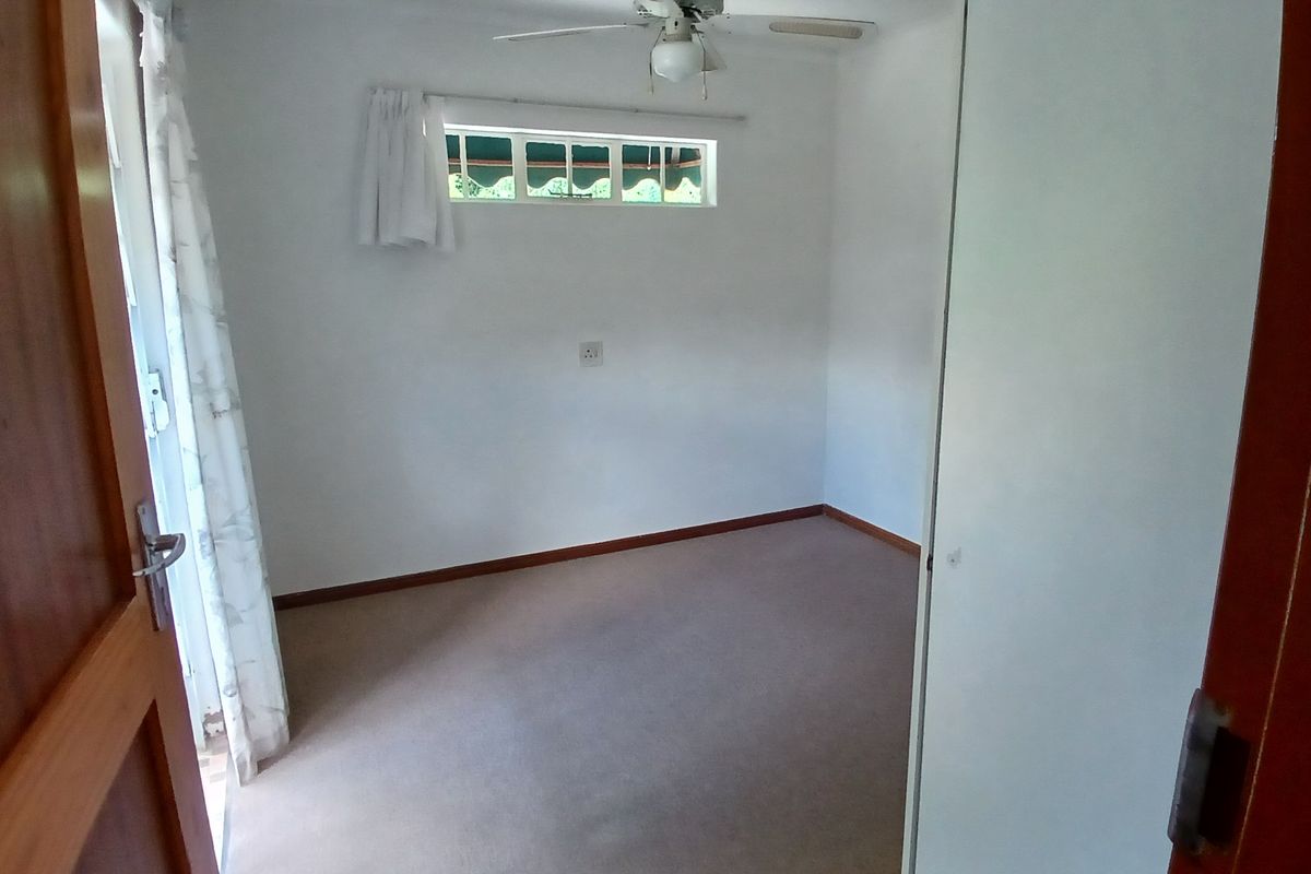 A vacant bedroom featuring neutral carpeting, a ceiling fan, and a small horizontal window, offering a clean and simple space ready for personalization.
