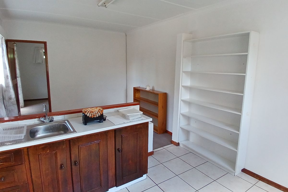 A functional kitchen area featuring wooden cabinetry, a stainless steel sink, and built-in shelving, offering a practical layout for daily use.