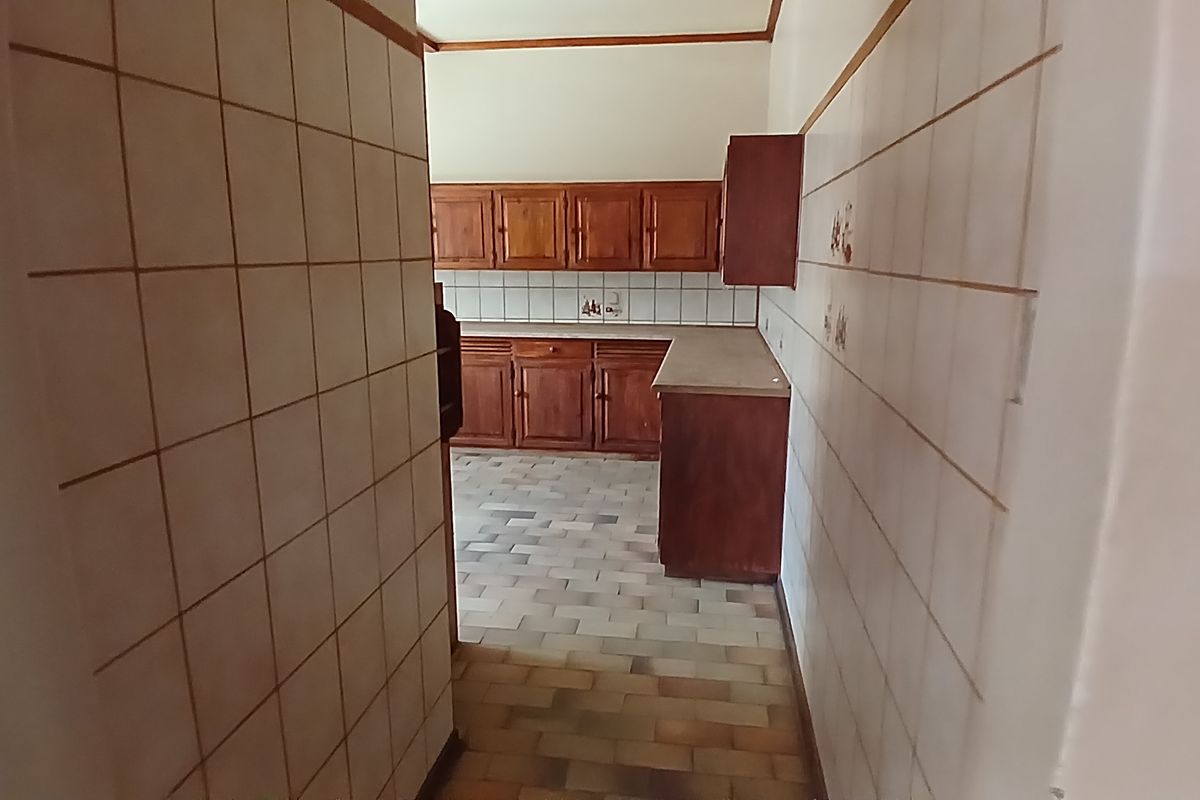 A dated kitchen featuring wooden cabinetry, tiled walls, and tiled flooring, offering a functional layout ready for modernization.