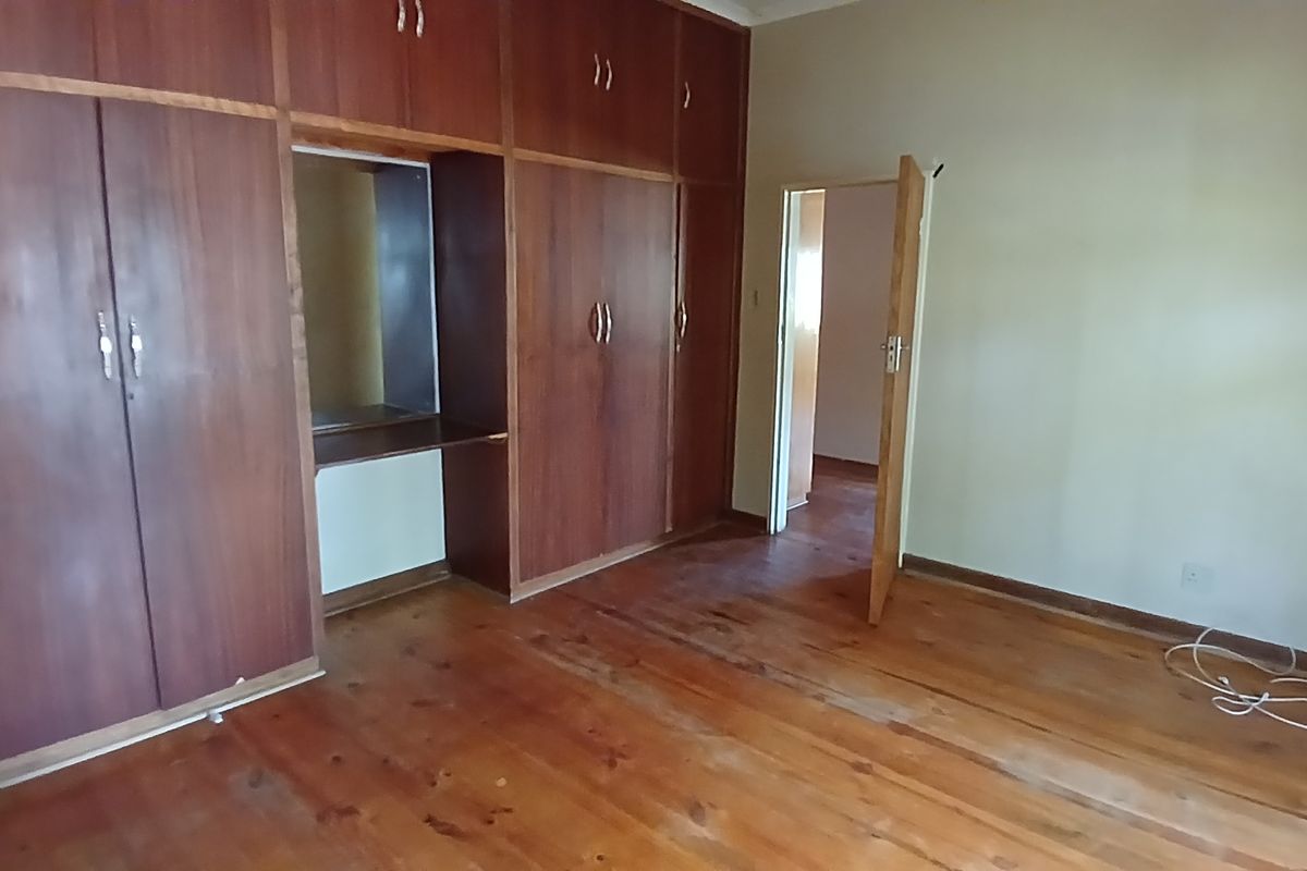 A bedroom featuring extensive built-in wooden cabinetry with a vanity nook and polished timber flooring.