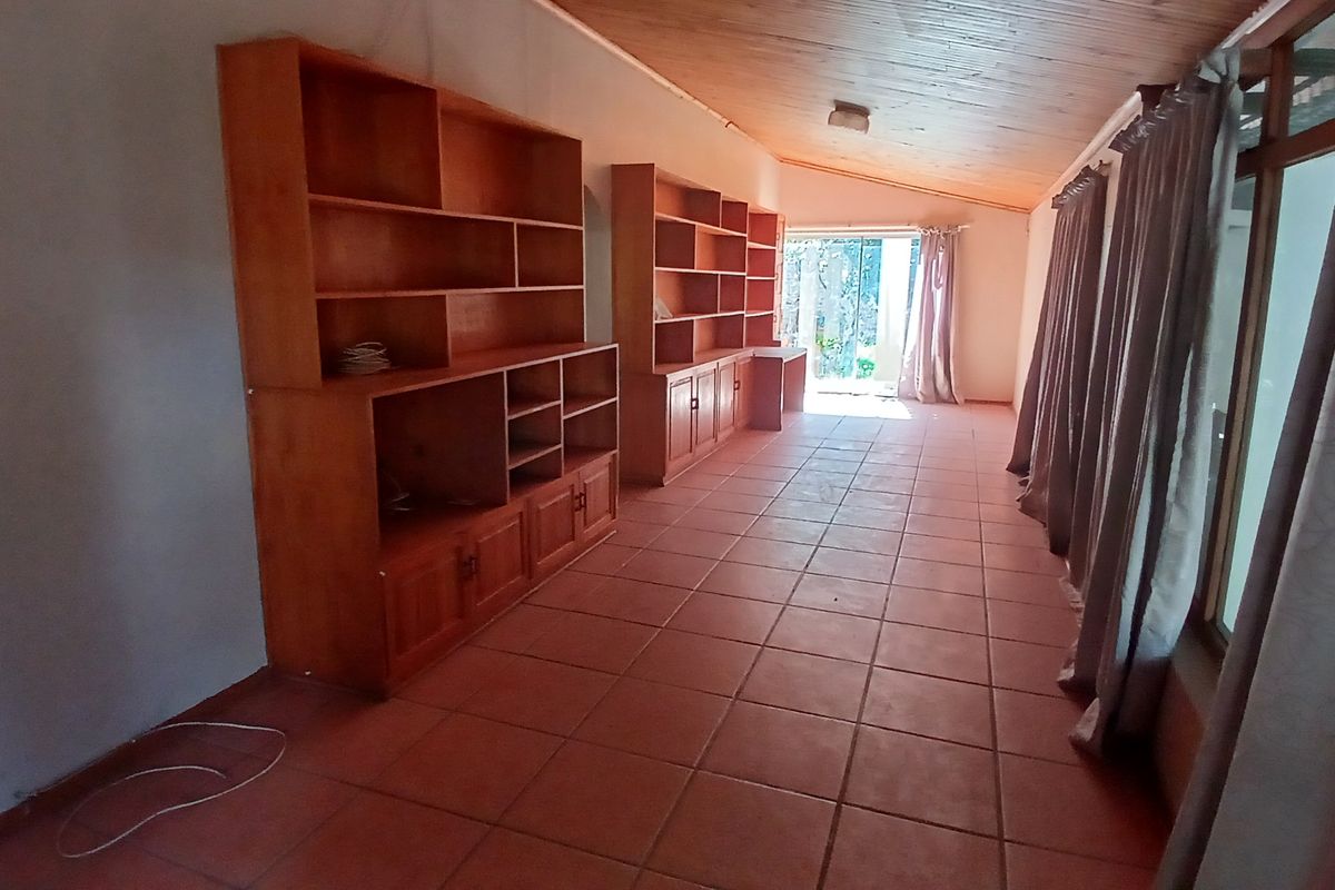 Spacious living area featuring built-in wooden shelving units, terracotta floor tiles, and a timber-clad ceiling with access to the outdoor area.