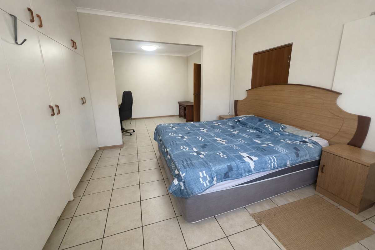 Spacious bedroom featuring built-in cupboards, tiled flooring, and an adjoining study or dressing area.
