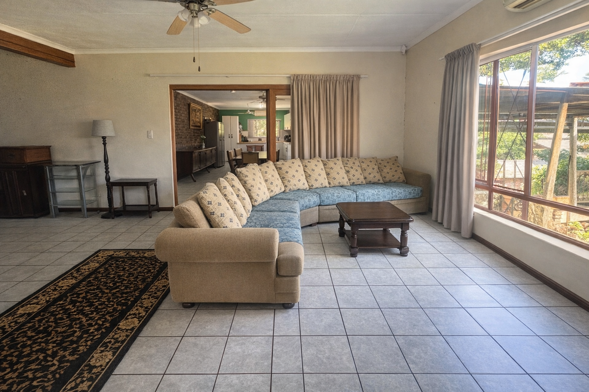 Spacious living room featuring large windows, tiled flooring, and a ceiling fan, with an open transition to the adjacent dining and kitchen area.