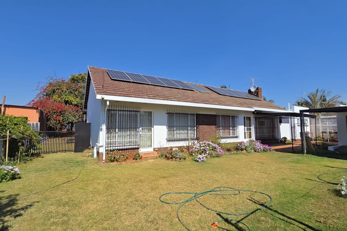 Rear view of the house featuring a well-maintained lawn, brick and white facade, and roof-mounted solar panels.