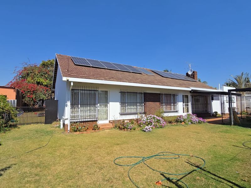 Rear view of the house featuring a well-maintained lawn, brick and white facade, and roof-mounted solar panels.