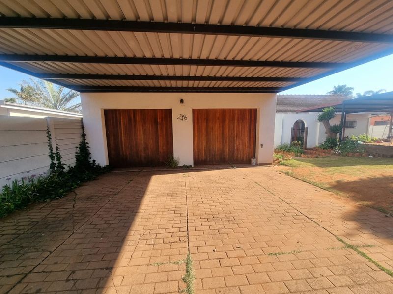 A double garage with wooden doors and a covered carport, featuring a paved driveway and boundary wall.