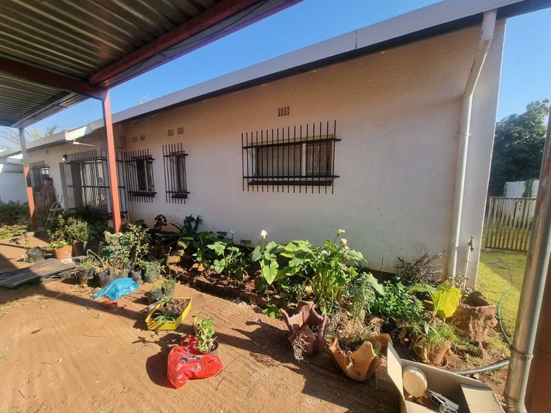Rear exterior view of the house featuring a covered patio area, security bars on windows, and an established garden bed along the wall.