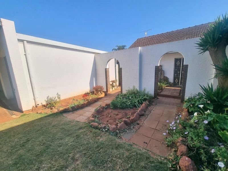 A rear courtyard area featuring arched architectural details, paved walkways, and established garden beds with stone borders leading to a secure entrance.