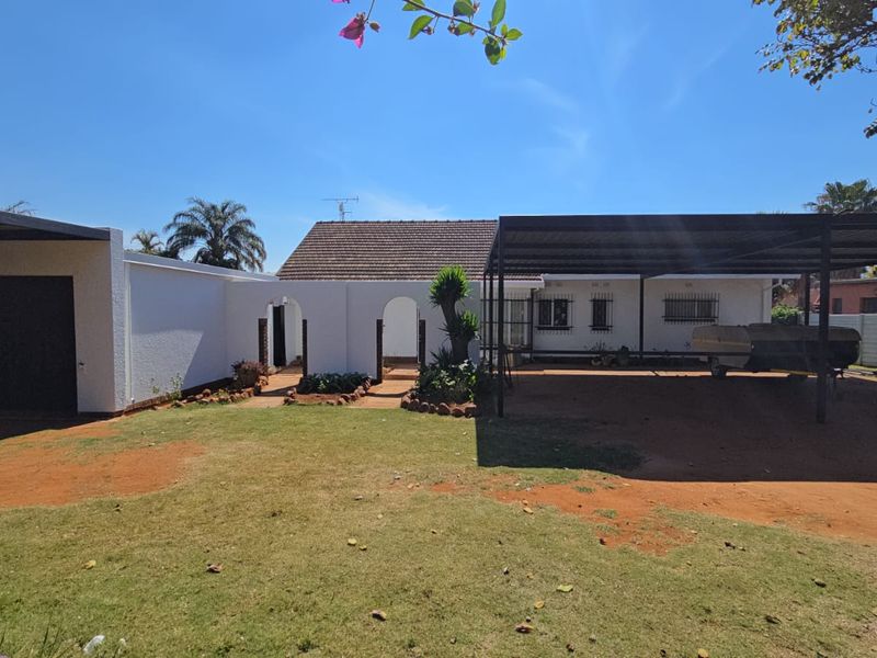 Rear view of the property featuring a large carport, garage, and a spacious garden area with paved pathways.