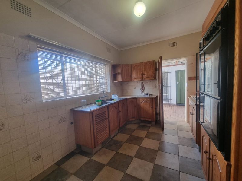 A dated kitchen featuring wooden cabinetry, tiled backsplash, and built-in oven, offering a functional layout with potential for modern renovation.