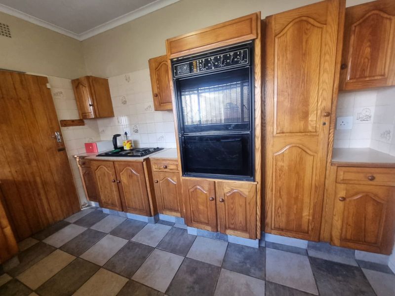 A functional kitchen featuring traditional wooden cabinetry, a built-in double oven, integrated hob, and tiled flooring with a neutral splashback.