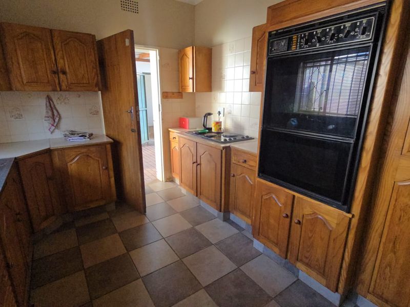 A functional kitchen featuring traditional wooden cabinetry, a built-in double oven, a hob, and tiled flooring, offering potential for a modern renovation.