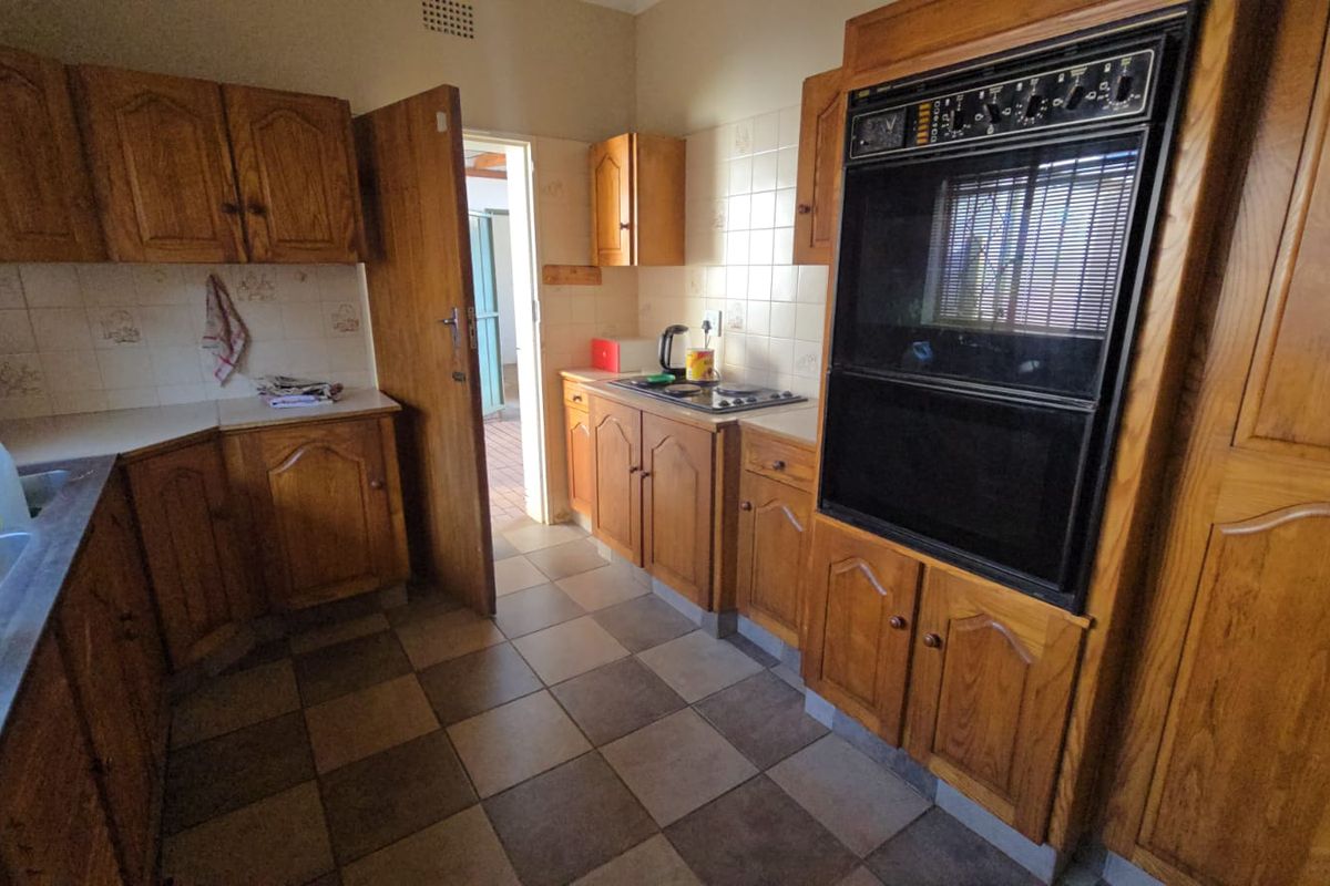 A functional kitchen featuring traditional wooden cabinetry, a built-in double oven, a hob, and tiled flooring, offering potential for a modern renovation.
