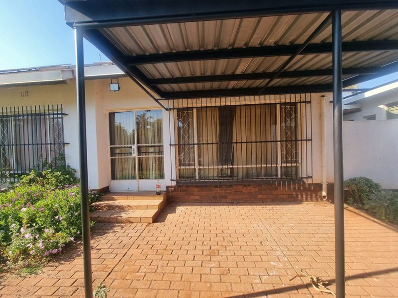 A covered patio area featuring brick paving, a metal carport structure, and security bars on the windows and sliding glass door.