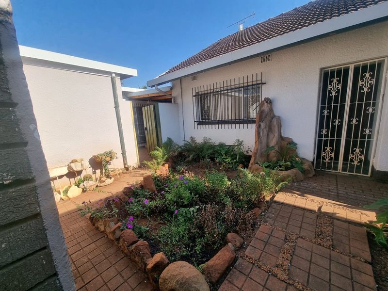 A paved rear courtyard featuring a raised garden bed, decorative rock feature, and secure access points with security bars and gates.