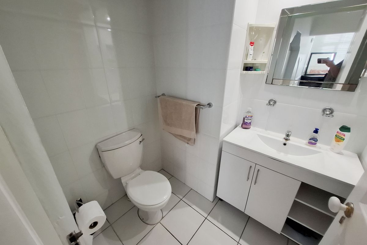 A functional bathroom featuring a white vanity cabinet, ceramic basin, wall-mounted mirror, and tiled finishes throughout.