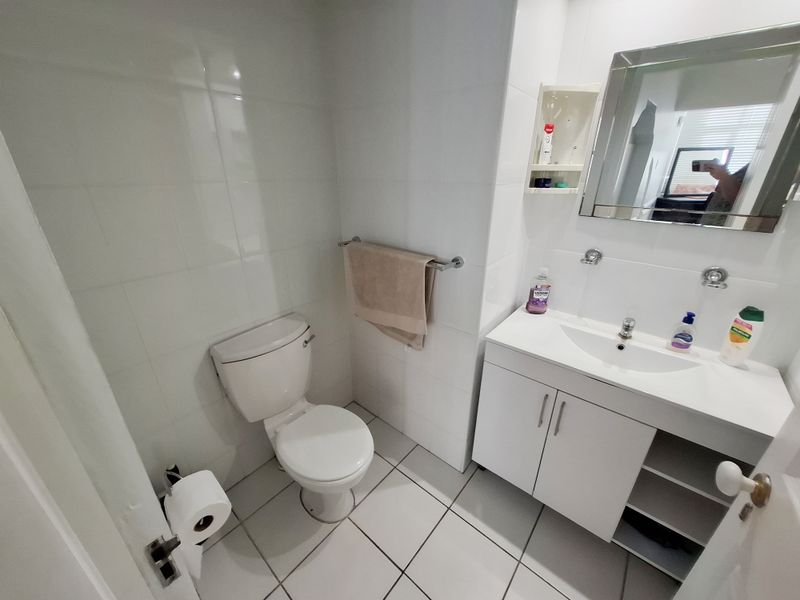 A functional bathroom featuring a white vanity cabinet, ceramic basin, wall-mounted mirror, and tiled finishes throughout.
