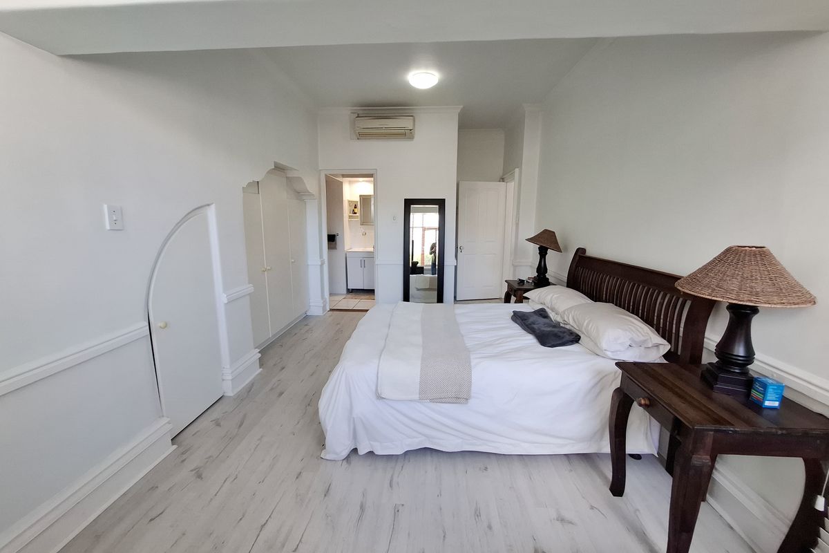 Spacious bedroom featuring light laminate flooring, built-in cupboards with unique arch detailing, and a wall-mounted air conditioning unit with an adjoining en-suite bathroom.