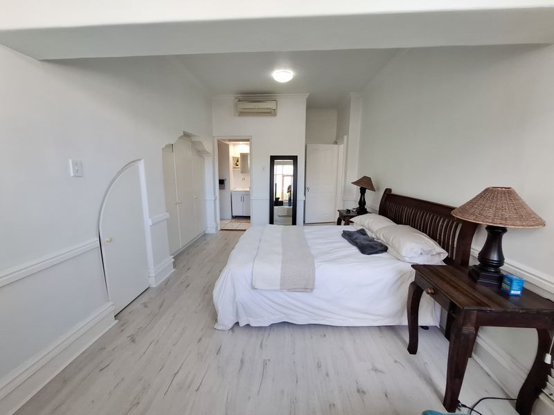 Spacious bedroom featuring light laminate flooring, built-in cupboards with unique arch detailing, and a wall-mounted air conditioning unit with an adjoining en-suite bathroom.