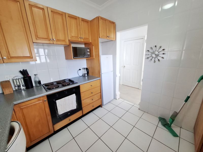 A functional kitchen featuring wooden cabinetry, tiled backsplash, and built-in appliances including an oven and hob, with tiled flooring throughout.
