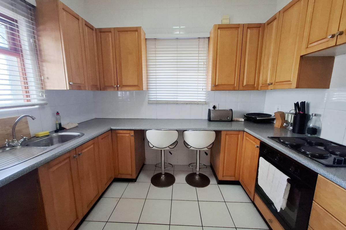 A functional kitchen featuring wooden cabinetry, laminate countertops, a built-in oven with electric hob, and tiled flooring with a breakfast bar area.