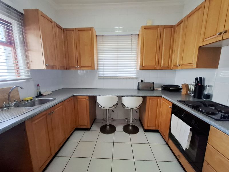 A functional kitchen featuring wooden cabinetry, laminate countertops, a built-in oven with electric hob, and tiled flooring with a breakfast bar area.