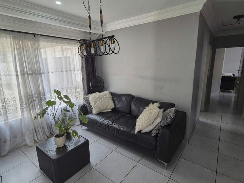 A living room featuring tiled flooring, crown molding, and a modern pendant light fixture, with access to an adjacent hallway.