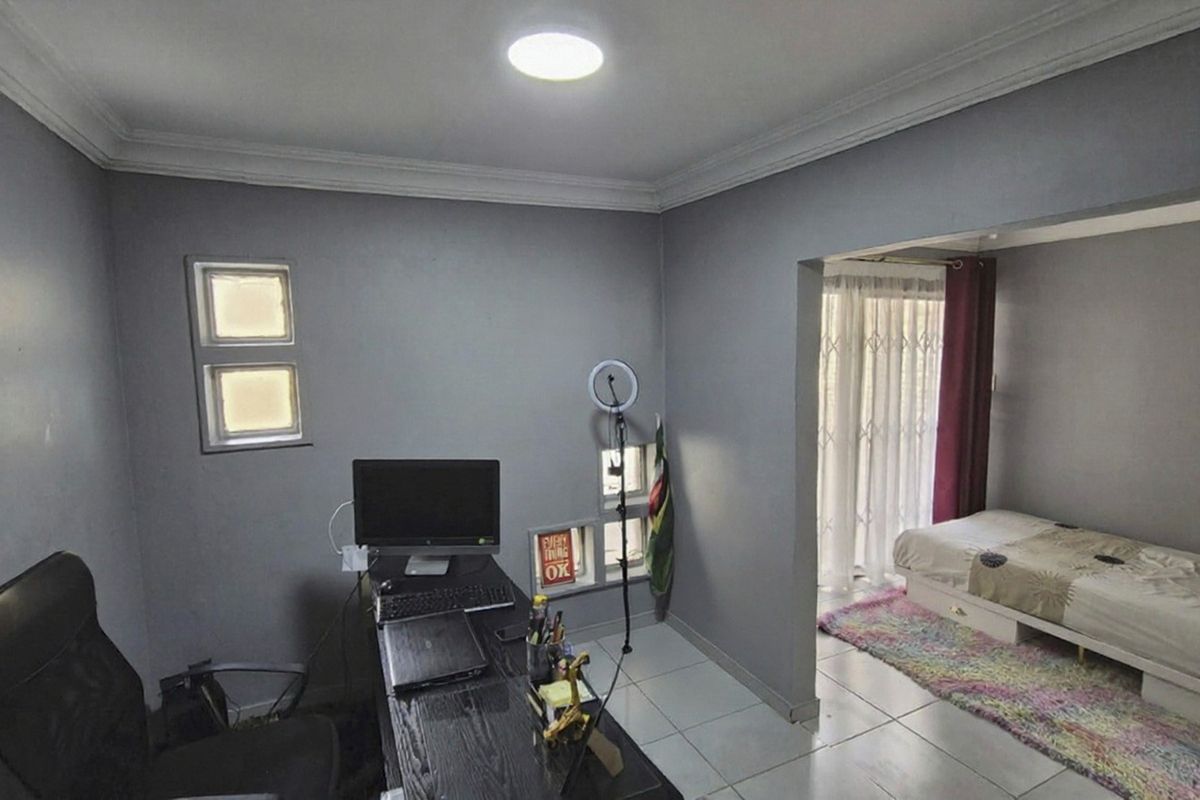 A multi-functional bedroom space featuring tiled flooring, coved ceilings, and a partitioned area with access to a patio through a security gate.