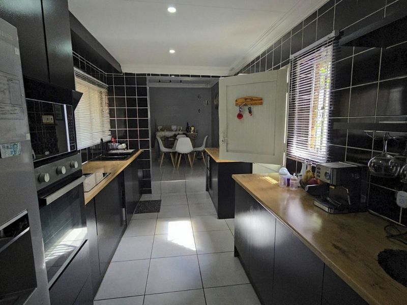 Modern galley-style kitchen featuring dark cabinetry, wooden countertops, tiled splashbacks, and integrated appliances, leading into an adjacent dining area.