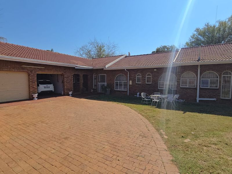 Front view of a single-story brick house featuring a paved driveway, attached garage, and arched windows set within a landscaped garden area.