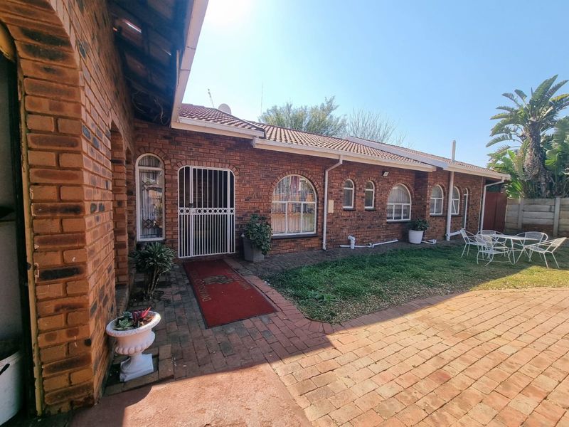 A rear exterior view of a face brick house featuring arched windows, a security gate, and a paved patio area leading to a small garden.