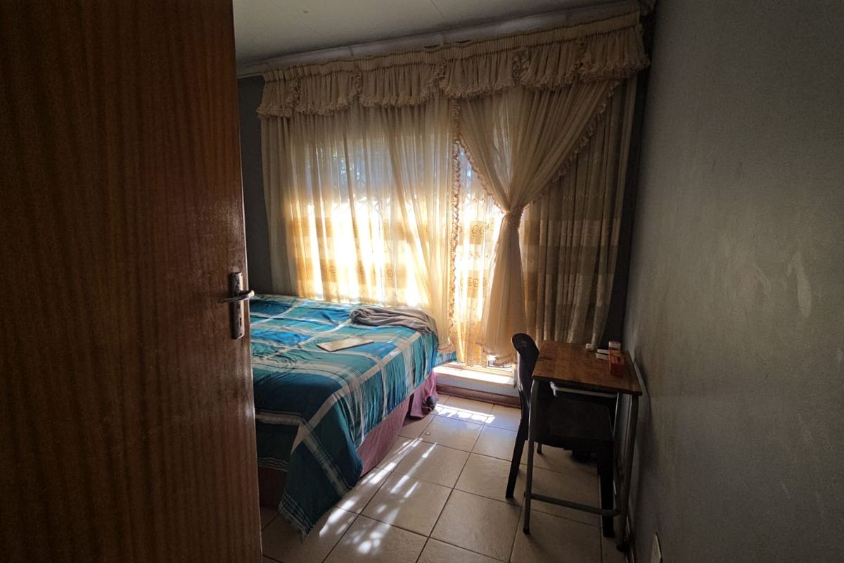 A compact bedroom featuring tiled flooring and natural light through window curtains, requiring cosmetic updates to improve the overall aesthetic.