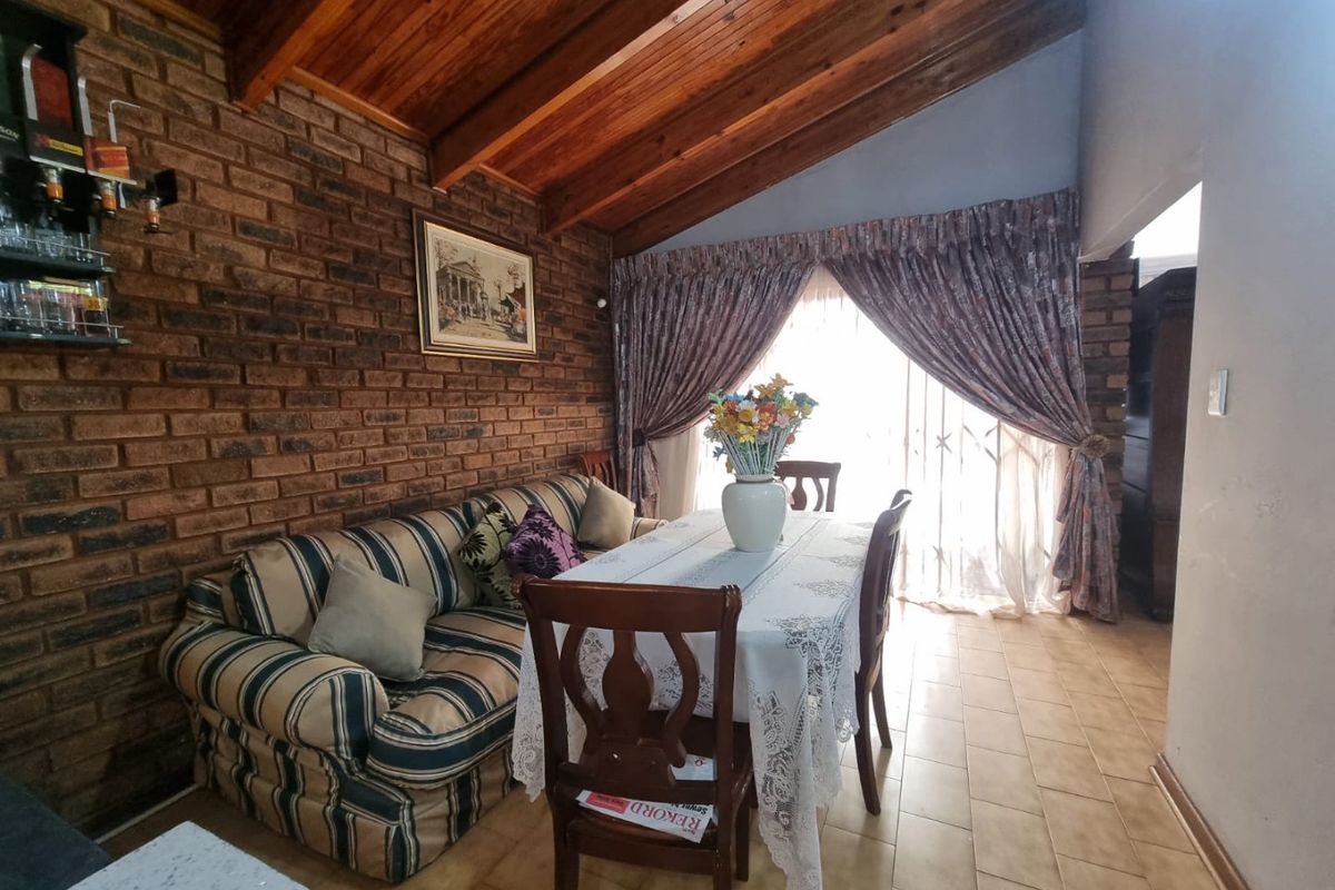 A living area featuring an exposed brick wall, vaulted timber ceiling, and tiled flooring with access to the outdoors via a sliding glass door.