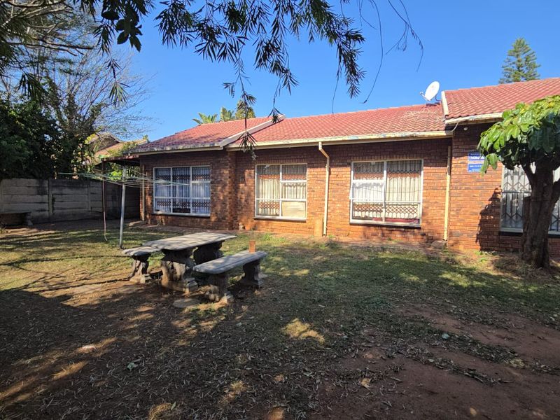 Rear view of a single-story brick house featuring a tiled roof, security bars on windows, and a spacious backyard with a boundary wall.