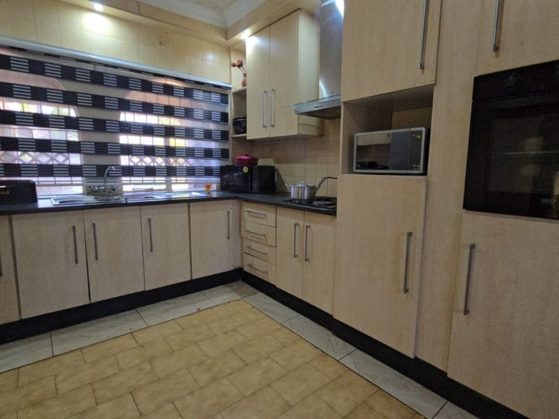 A functional kitchen featuring light wood-finish cabinetry, dark countertops, built-in oven, extractor fan, and tiled flooring with a tiled backsplash.