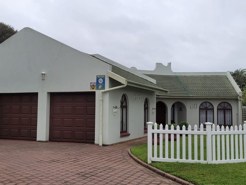 Front elevation of a residential property featuring a double garage, paved driveway, arched windows, and a white picket fence enclosing the front garden.