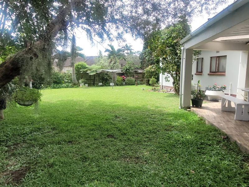 A spacious rear garden featuring a well-maintained lawn, mature trees, and a covered patio area with tiled flooring.