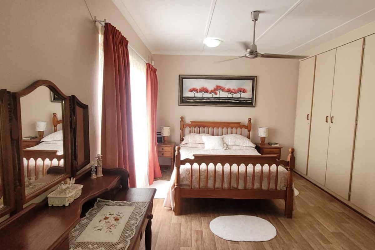 A well-maintained bedroom featuring extensive built-in cupboards, a ceiling fan, and durable laminate flooring, offering a functional and comfortable living space.