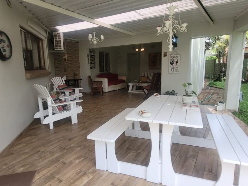 A spacious covered patio featuring tiled flooring and translucent roof panels, providing a seamless transition to the garden area.