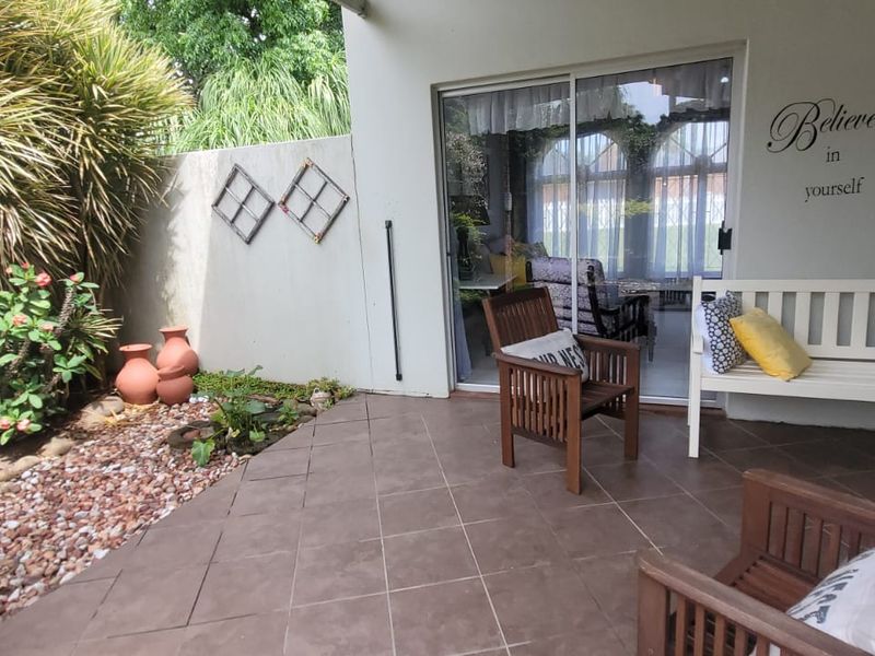 A covered patio area featuring tiled flooring, a brick pillar, and a sliding glass door providing access to the interior living space.